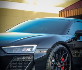 Close-up of a black sports car's front-left quarter, showing a sharp headlight, large grille, and red brake calipers; Blue Star Auto Salon logo in the corner.