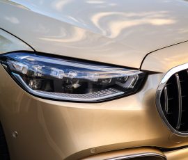 Close-up of a gold car front, showing the headlight, grille, and bumper.