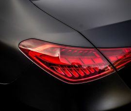 Close-up of a dark car's rear corner, showing a red taillight and black body with a BlueStar Autosalon watermark in the lower corner.