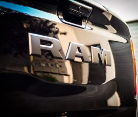 Close-up of the chrome RAM badge on the rear of a black pickup, with reflections of the surroundings on the surface.