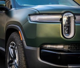 Front-left view of a green Rivian SUV showing the distinctive vertical grille badge and headlight detail.