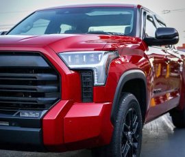 Red pickup truck in a three-quarter front view with a bold black grille and LED headlights; Blue Star Autosalon watermark in the corner.