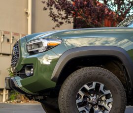 Front-left close-up of a green pickup truck showing headlight, fender, and rugged tire; Blue Star Autosalon logo in the lower corner.