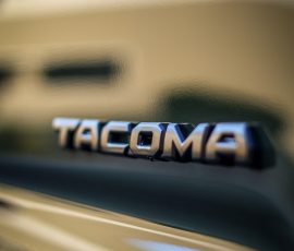 Close-up of a chrome TACOMA badge on a gold car, reflections visible, with Bluestar Autosalon watermark in the bottom-right corner.